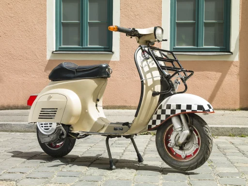 Cremefarbene Vespa V50N Baujahr 1973 mit Frontgepäckträger und Schachbrettmuster am Kotflügel.
