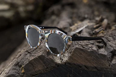 Designer-Sonnenbrille mit gemustertem Rahmen auf einem Baumstamm in einer professionellen Lifestyle-Produktaufnahme.
