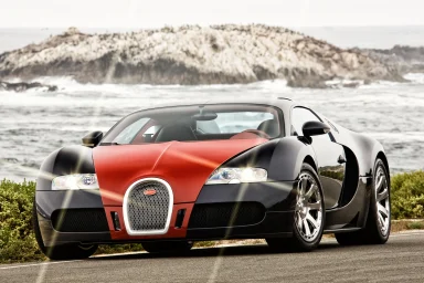 Bugatti Veyron Supersportwagen in schwarz-rot vor Küstenlandschaft mit Wellen und Felsen.