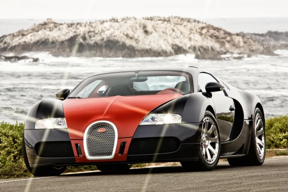 Bugatti Veyron Supersportwagen in schwarz-rot vor Küstenlandschaft mit Wellen und Felsen.