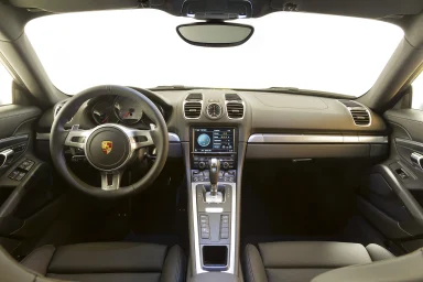Cockpit eines Porsche Cayman mit Sportlenkrad, Mittelkonsole und schwarzer Lederausstattung in symmetrischer Frontalansicht.