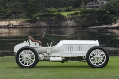 Weißer Oldtimer-Rennwagen mit braunem Lederinterieur am Wasser.