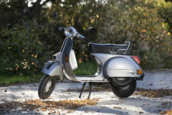 Silberne Vespa PX 125 E Lusso Baujahr 1994 mit fliegenden Herbstblättern.
