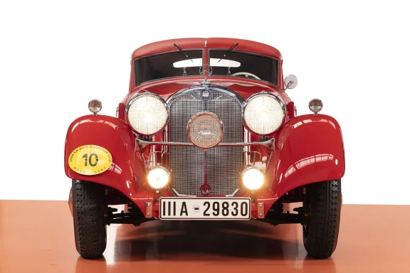 Frontansicht eines roten Mercedes-Benz 540 K Stromlinien-Coupés mit eingeschalteten Hauptscheinwerfern vor neutralem Hintergrund.