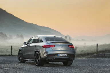 SilbernerMercedes-AMG GLE 63 S 4MATIC+ Coupé auf einer Landstraße bei Morgennebel und bewaldeten Hügeln im Hintergrund.