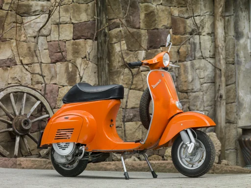 Orange Vespa 50 R (V5A1T) vor einer historischen Natursteinmauer.