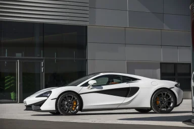 Weißer McLaren 570S vor moderner Architektur in Seitenansicht.