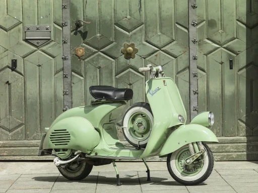 Hellgrüne Vespa ACMA V55 Baujahr 1955 mit Reserverad vor einem historischen Holztor.
