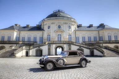 Ein klassisches Auto vor einem eleganten historischen Gebäude mit Treppen.