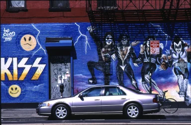 Graffiti-Wand mit KISS-Motiv, davor ein silberner Cadillac.