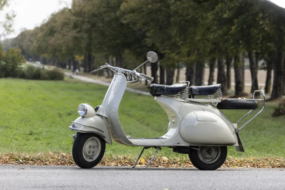 Weiße Vespa Faro Basso Baujahr 1957 auf einer ruhigen Landstraße.

