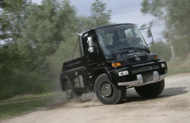 Schwarzer Mercedes-Benz Unimog Brabus fährt dynamisch über eine Schotterstraße und wirbelt Staub auf.
