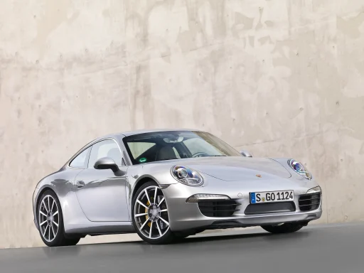 Silbermetallic lackierter Porsche 911 Carrera mit markanten gelben Bremssätteln vor einer Betonmauer.