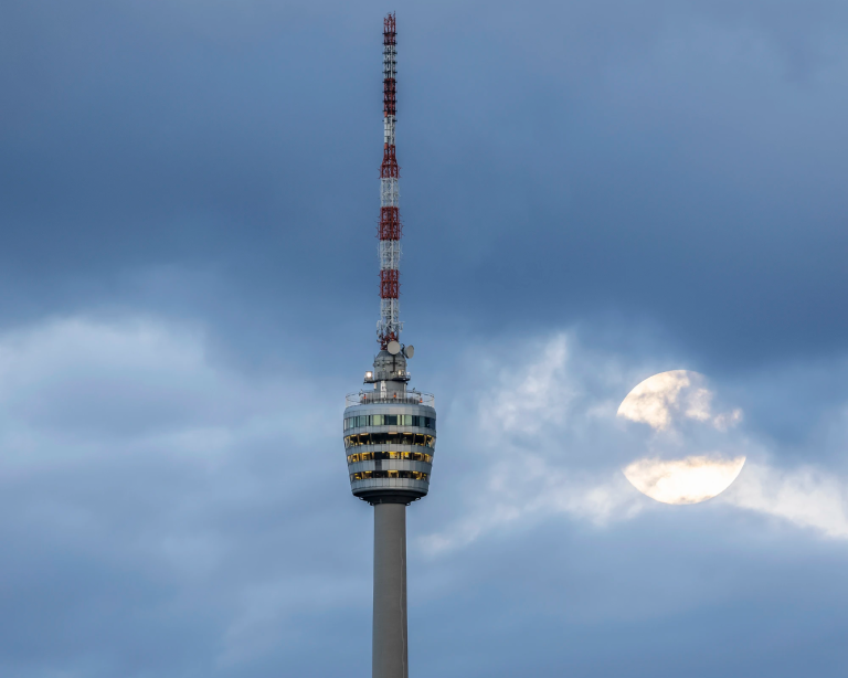 Fernsehturm Stuttgart mit Mond vor einem wolkenverhangenen Abendhimmel.