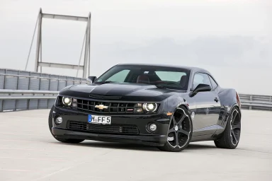 Schwarzer Chevrolet Camaro auf einem Parkplatz mit Brücke im Hintergrund.