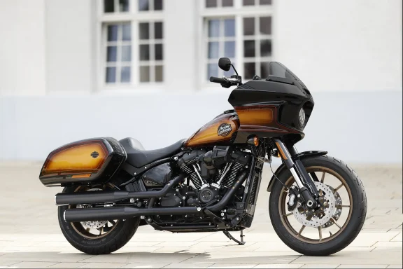 Harley-Davidson Low Rider ST FXLRST 2024 in Tobacco Fade mit Frontverkleidung und Seitenkoffern, fotografiert vor moderner Architektur.