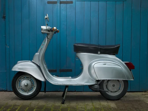 Silberne Vespa 50 Special vor einem blauen Holztor.
