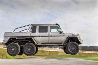 Mercedes-AMG G 63 6x6 in Seitenansicht während einer dynamischen Fahrt auf einer Straße, mit ländlicher Landschaft und bewölktem Himmel.