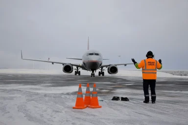 Flugzeug auf dem verschneiten Flughafen von Arjeplog mit Einweiser auf dem Vorfeld bei winterlichen Bedingungen.