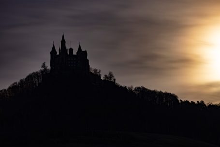 Burg Hohenzollern im Gegenlicht als Silhouette auf einem bewaldeten Berg.