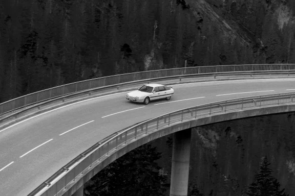 Citroën CX 25 GTI Turbo in Schwarzweiß auf einer geschwungenen Brücke in den Alpen.