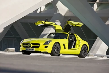 Gelber Mercedes SLS AMG E-Cell mit offenen Flügeltüren, geparkt vor moderner Architektur