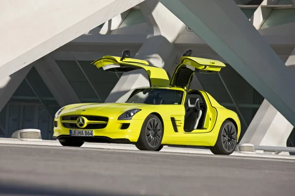 Gelber Mercedes SLS AMG E-Cell mit offenen Flügeltüren, geparkt vor moderner Architektur