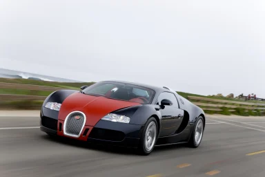 Schwarz-roter Bugatti Veyron in dynamischer Fahrt entlang einer Küstenstraße.