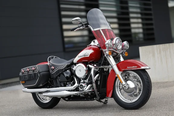 Harley-Davidson Hydra-Glide Revival FLH 2024 in Redline Red mit Windschutzscheibe und Ledertaschen, fotografiert vor moderner Architektur.

