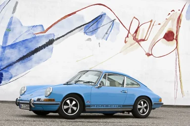 Blauer Porsche 911 vor einer bunten, abstrakten Wandmalerei.