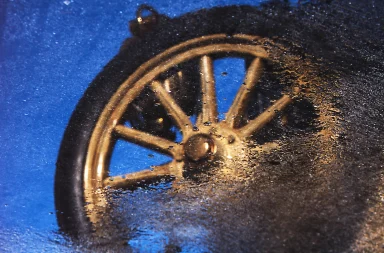 Abstrakte Reflexion eines automobilen Speichenrades auf einer nassen Oberfläche mit Wassertröpfchen und blauer Farbgebung.