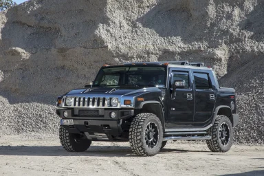 Schwarzer Hummer H2 mit Offroad-Bereifung, fotografiert vor Kiesbergen in einer industriellen Umgebung.