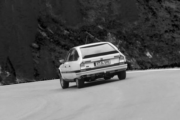 Heckansicht einesCitroën CX 25 GTI Turbo in Schwarzweiß auf einer kurvenreichen Alpenstraße mit Bergkulisse.