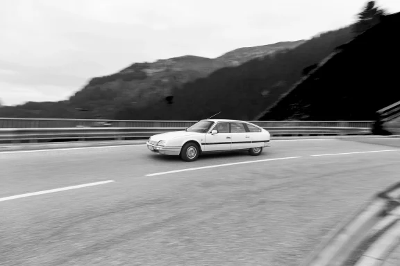 Citroën CX 25 GTI Turbo als Schwarzweiß-Fahraufnahme auf einer Alpenstraße mit Bergkulisse.
