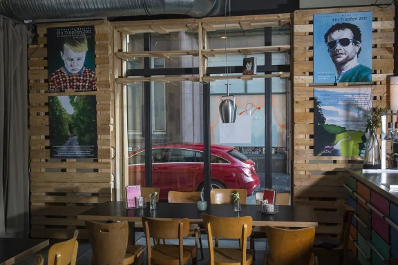 Blick aus einem Restaurant durch das Fenster auf einen roten Mercedes-Benz CLA vor dem Gebäude – stimmungsvoller Automobil-Moment.