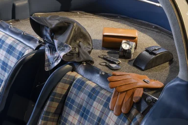 Lederhandschuhe, Ledermütze, Armbanduhr und weitere Accessoires im Innenraum eines klassischen Fahrzeugs.