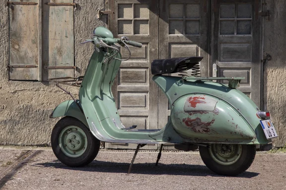 Grüne Vespa 125 U Baujahr 1953 mit originaler Patina vor historischer Fassade.
