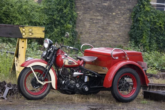 Professionelle Aufnahme des Harley-Davidson Servi-Car von 1943 vor einer historischen Industrie- und Bahnanlage. Ein seltener Klassiker der 