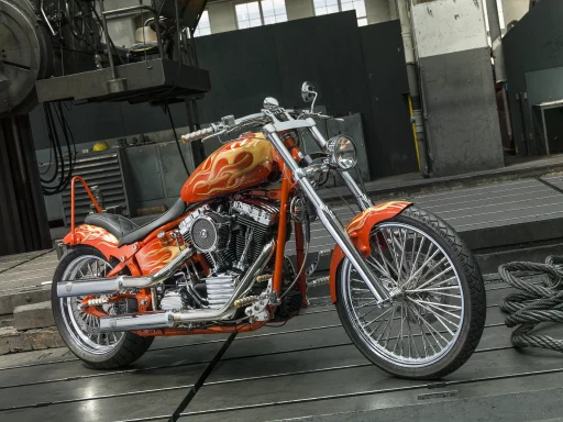 Custom Harley-Davidson FXSTD Deuce Billy Bike von 2003 mit Flammenlackierung und langem Gabelumbau vor industrieller Kulisse.
