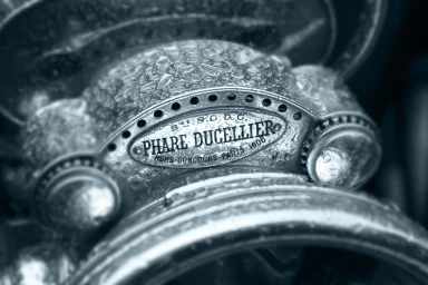 Detail eines historischen Automobils mit Phare-Ducellier-Scheinwerfer und Regentropfen.