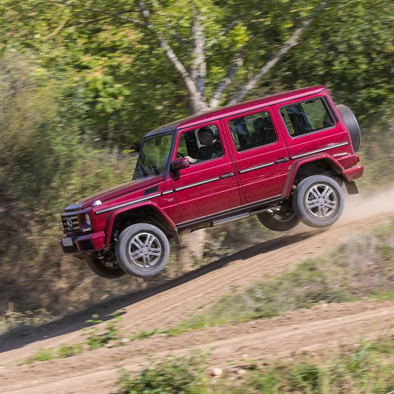 Rote Mercedes-Benz G-Klasse bei einem Offroad-Sprung auf einer staubigen Geländestrecke.