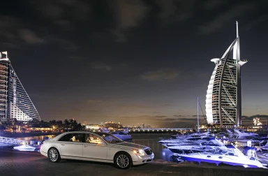 weisser Maybach 62s vor dem Burj Al Arab und beleuchteten Yachten am Abend.
