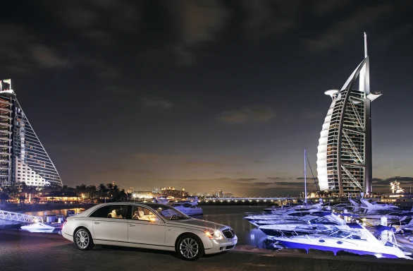 weisser Maybach 62s vor dem Burj Al Arab und beleuchteten Yachten am Abend.