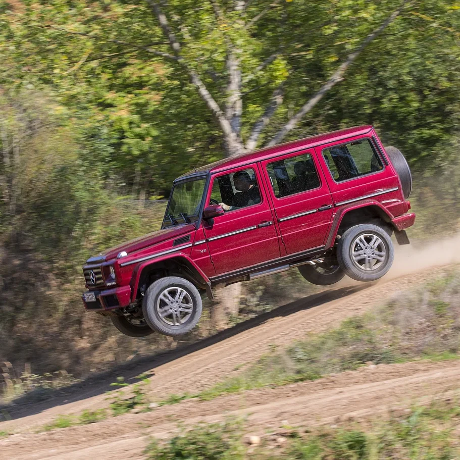 Rote Mercedes-Benz G-Klasse bei einem Offroad-Sprung auf einer staubigen Geländestrecke.
