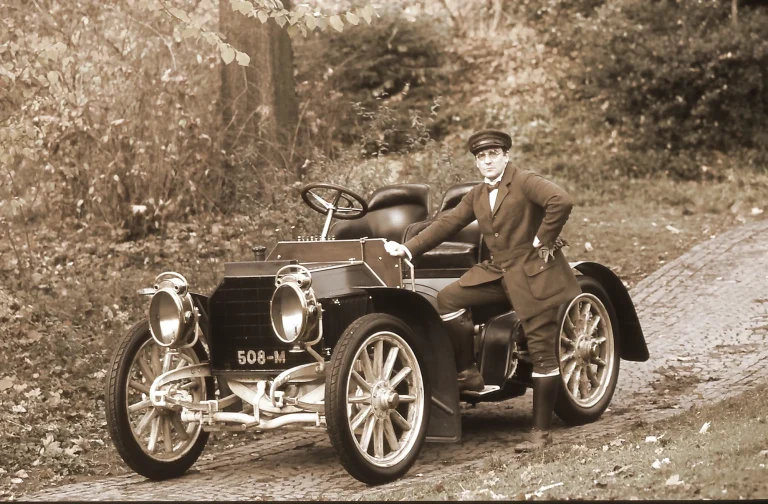 Mercedes Simplex 1902 Oldtimer Chauffeur Classic Fotografie Historischer Mercedes Simplex von 1902 mit Chauffeur in zeitgenössischer Kleidung auf einer Kopfsteinpflasterstraße.