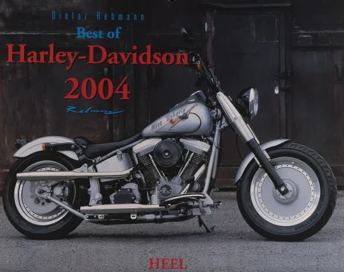 Harley-Davidson Softail Fat Boy mit „Miss Behavin'“-Tankdesign in Seitenansicht vor dunkler Industriehalle.Harley Kalender 2004