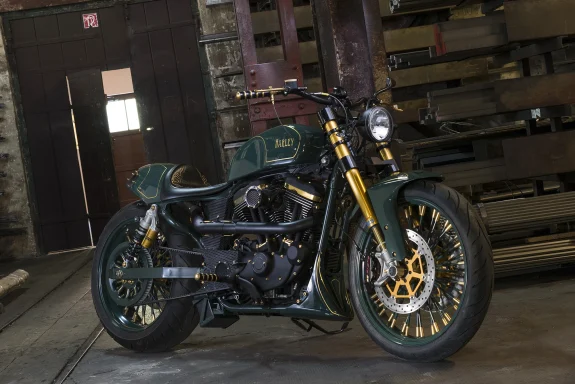 Harley-Davidson Sportster XL1200 Custom Café Racer Baujahr 2010 in Grün und Gold, fotografiert in einer historischen Industriehalle.