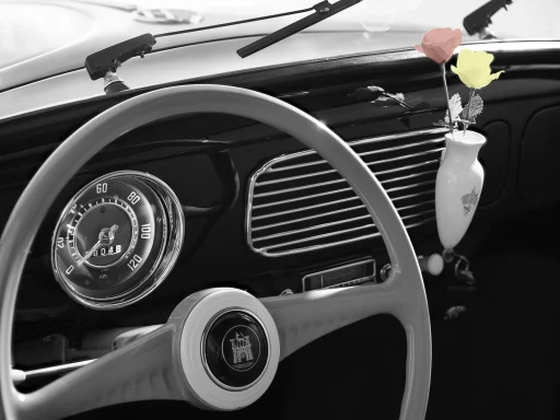 Innenraum eines klassischen Volkswagen Käfers mit weißem Lenkrad, geöffneten Türen und schlichtem Armaturenbrett in Schwarz-Weiß-Darstellung